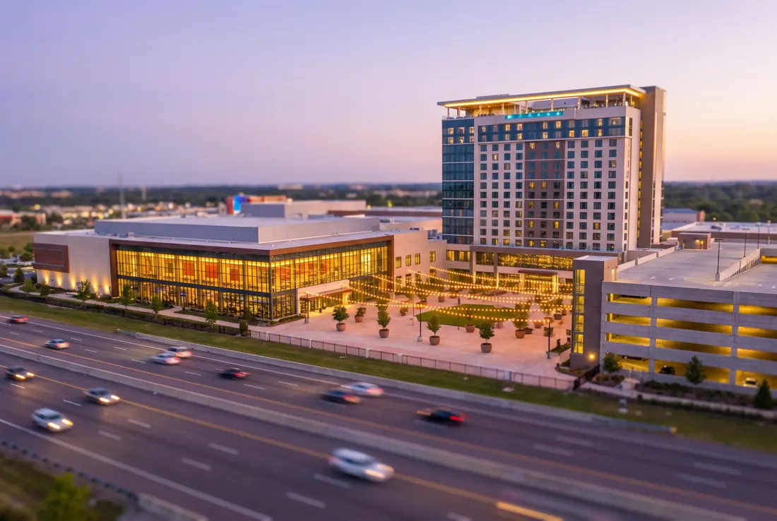 Tilt-shift miniature of a large glass-fronted entertainment resort with a hotel tower beside a busy highway at dusk