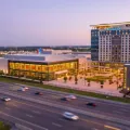 Tilt-shift miniature of a large glass-fronted entertainment resort with a hotel tower beside a busy highway at dusk